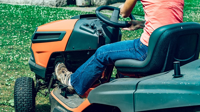 woman riding orange ride on lawnmower